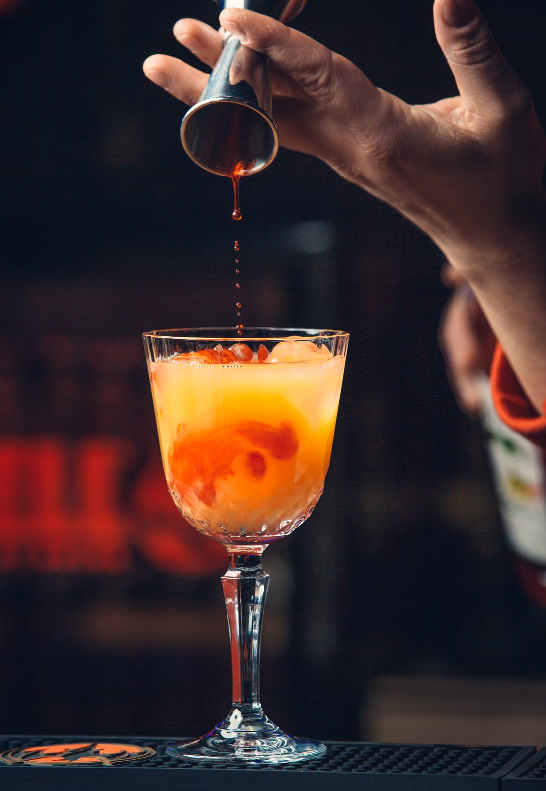 Un sirop rouge versé dans un cocktail à l'orange, au comptoir de Gaya